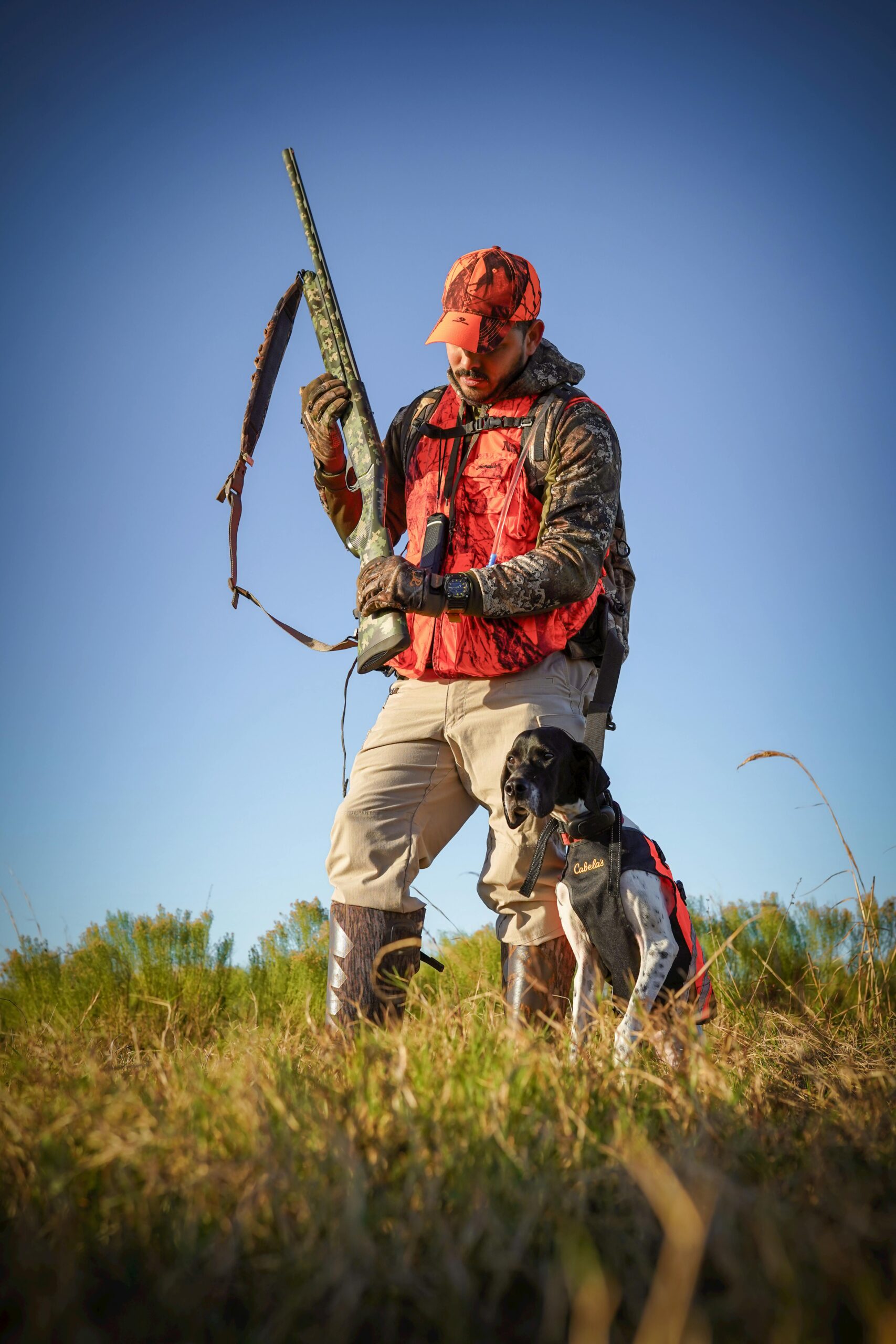 Hunter holding rifle with dog in sunny Florida field, showcasing outdoor hunting gear.
